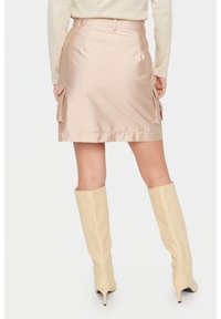 Ljust rosa satin kjol med sidofickor, åtsittande midja och kort skärning. Matchad med knähöga beige klackstövlar.