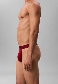 Roter Calvin Klein Tanga, der eine glatte Textur und ein schmales Design zeigt. Der Bund tr�ägt den Markennamen in einem subtilen, tonalen Druck.