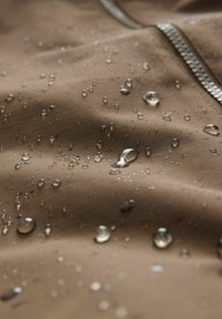 Tissu marron résistant à l'eau avec des gouttes visibles. Texture lisse et éclat subtil, avec une fermeture éclair argentée le long d'un bord.