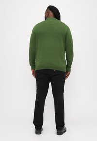 Zelený sveter s okrúhlym výstrihom, rebrovanými manžetami a lemom. Skombinovaný s čiernymi nohavicami rovného strihu a čiernymi topánkami, zobrazený zozadu.