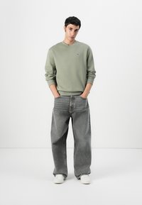Groene katoenen sweatshirt met lange mouwen, gecombineerd met losse grijze spijkerbroek en witte sneakers. Eenvoudig ontwerp, minimale branding.