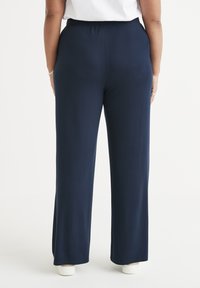 Navyblauwe broek met eenwide-leg ontwerp, gemaakt van een soepele, stretchy stof. Heeft een elastische tailleband en subtiele zijnaad.