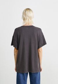 Tmavošedé oversized tričko s krátkymi rukávmi, surovými okrajmi a voľným strihom. Materiál vyzerá mäkko s jemne opotrebovanou textúrou.
