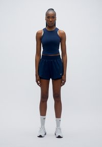 Marineblå atletisk crop top og shorts, lavet af åndbart stof, kombineret med hvide Nike-sokker og sko, med et minimalistisk design og logoaccents.