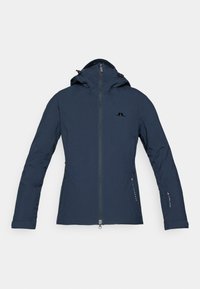 Chaqueta aislante azul marino con capucha, cierre frontal y bolsillos laterales con cremallera. Presenta un logo sutil y una textura de tela resistente.