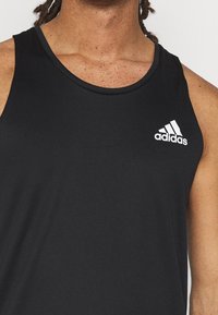 Top di allenamento nero realizzato in tessuto liscio, con scollatura rotonda e logo Adidas bianco sul lato sinistro del petto.