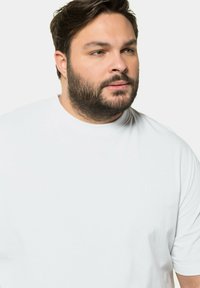 T-shirt bianco a maniche corte realizzato in morbido cotone, con scollatura rotonda e un logo in rilievo discreto sulla parte anteriore.