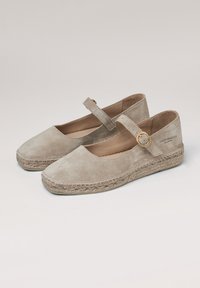 Zapatos planos de ante beige con puntera redonda, correa en el tobillo y suela decorativa de esparto tejido. Accento de hardware dorado simple en la correa.