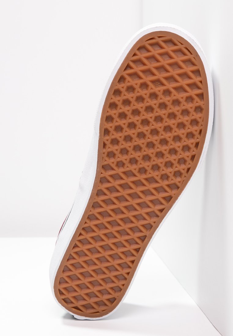 Suela de zapato de goma con un patrón texturizado de panal en marrón, que presenta una parte superior de tela blanca con una ligera curvatura a lo largo de los bordes.