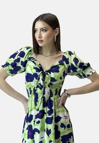 Kleid mit Blumenmuster in Grün, Marineblau und Pink, mit Puffärmeln, gerüschtem Oberteil und einer Bindeschleife vorne. Glattes Material mit fließender Silhouette.