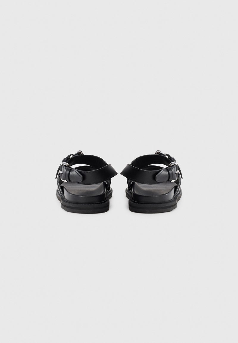 Black leather sandals featuring two adjustable straps with metal buckles and a flat, textured sole. Rear view shows open heel design.