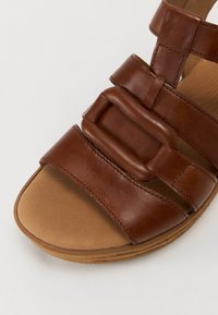 Sandalo in pelle marrone con pettini larghi e fibbia rettangolare. Soletta imbottita con punta arrotondata e suola testurizzata.