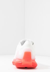 Chaussure de sport blanche avec une tige texturée, une semelle dégradée du rose au blanc, et un talon prononcé pour le support et l'amorti.