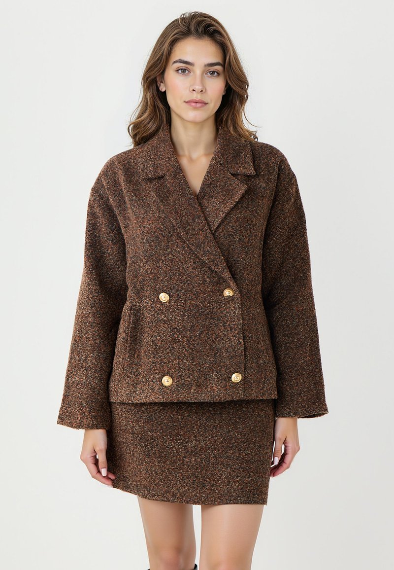 Braune strukturierte Doppelreiherjacke mit großen goldenen Knöpfen, breiten Revers und leicht übergroßen Ärmeln, kombiniert mit einem passenden Rock.