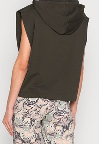 Bezramenný tmavě zelený zkrácený hoodie, který je nošen s kalhotami s vysokým pasem s pastelovým paisley a květinovým vzorem.