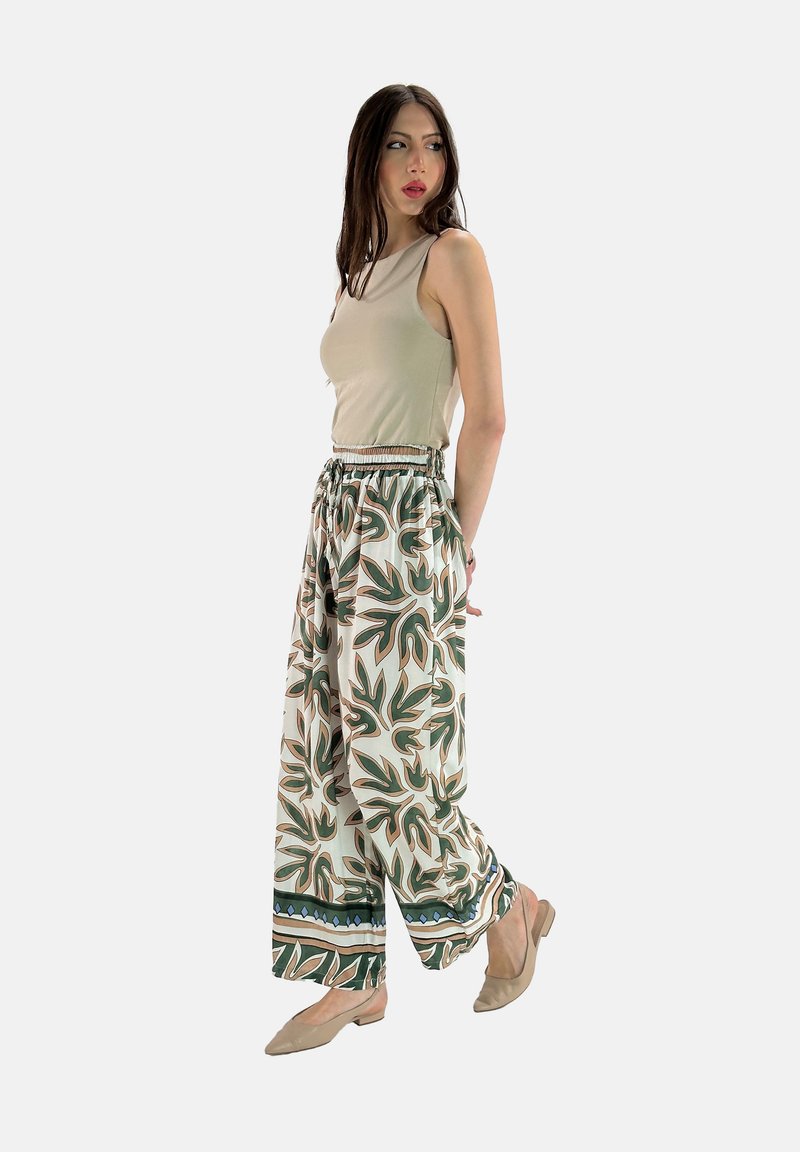 Relaxed-fit, gestreepte broek in het wit met groene en oranje bladdessins, gecombineerd met een beige mouwloos topje en lichtbruine ballerina's.
