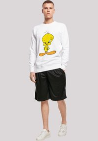 Hvit sweatshirt med et fargerikt Tweety Bird-motiv, kombinert med svarte shorts og hvite sneakers. Glatt stoff, avslappet design.