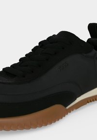 Baskets Adidas noires avec tige noire texturée, lacets noirs et semelle en caoutchouc couleur gomme avec bord strié visible sur fond blanc.