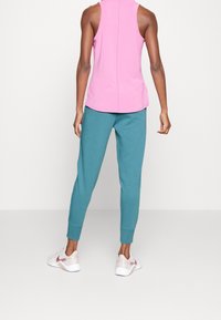 Rosa ärmelloses Oberteil und türkise Jogginghosen mit gerippten Bündchen, kombiniert mit weißen und rosa Sportschuhen. Glatte Texturen und schlichtes Design.