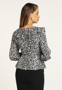 Grå bluse med lys og mørk dyreprint, flæset krave og lange puffede ærmer. Stoffet har en glat tekstur og en tætsiddende silhuet.