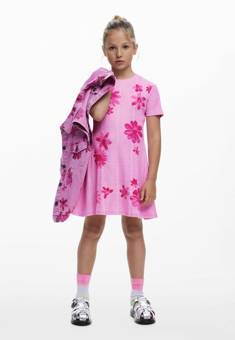 Rosa Kleid mit Blumenmuster, kurzen Ärmeln und lockerem Schnitt. Eine passende rosa Jeansjacke ist über den Arm gelegt. Silberne Sandalen.