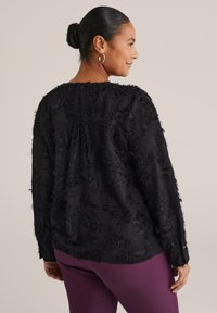 Top leggero nero a maniche lunghe con dettagli texture e sfrangiati; abbinato a pantaloni viola. Caratterizzato da una vestibilità rilassata e scollatura rotonda.