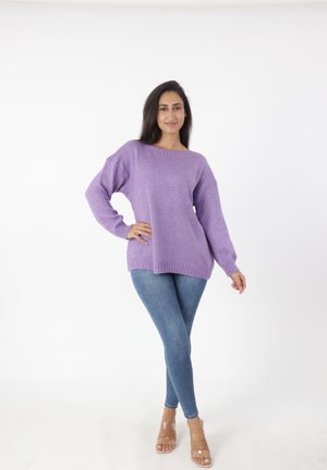 Paarse gebreide trui met een brede halslijn en een ribgebreide zoom, gecombineerd met strakke blauwe jeans en doorschijnende hakken. Smeuïge textuur.