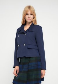 Στρατιωτικό cropped σακάκι σε υφασμάτινη υφή, με γιακά με χαραγμένη εγκοπή, διπλή σειρά ασημένιων κουμπιών και δύο μπροστινές τσέπες.