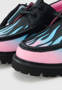 Chaussures en cuir noires et roses avec des semelles noires épaisses et des motifs de flammes bleues sur la partie avant supérieure.