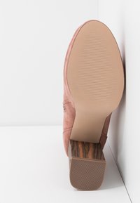 Chaussure en daim rose avec un talon bloc texturé marron. La semelle est lisse avec des rainures pour l'adhérence. Conçue avec un bout légèrement arrondi.