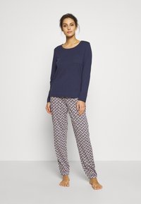 Haut à manches longues bleu marine avec une poche poitrine, associé à un pantalon ample à motifs avec un design en zigzag dans des couleurs claires et foncées.