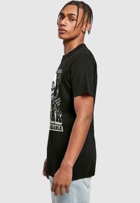 Black cotton t-shirt featuring a graphic design on the front, including bold text and an illustration, with short sleeves and a relaxed fit.