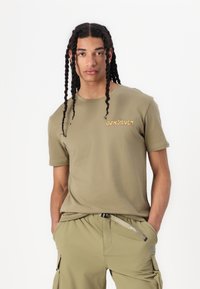 Olijfgroene katoenen t-shirt met korte mouwen, met "Quiksilver" in oranje gedrukt op de linker borst, met een zachte stoftextuur.