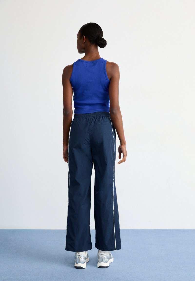 Blauwe mouwloze top en marineblauwe wijde broek met witte zijkanten. De outfit heeft een zachte textuur en een elastische taille. Zilveren sneakers maken de look compleet.
