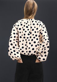 Garām piedurknēm, viegls tops gaiši rozā krāsā ar lieliem tumši ziliem punktiņiem; sakrātas kakla apkakles un apjomīgas piedurknes; tumšas piestiprinātas bikses.