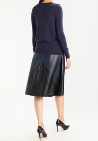 Marineblauwe trui gecombineerd met een zwarte leren rok met een geometrisch ontwerp. De outfit wordt aangevuld met zwarte hoge hakken.