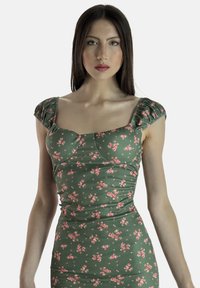 Zielona kwiatowa bluzka z prążkowanej tkaniny, z krótkimi bufkami, kwadratowym dekoltem i marszczonymi detalami. Całość w różowo-białym wzorze kwiatowym.