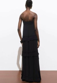 Black maxi dress with layered ruffles, strapless design, soft texture, and flowing silhouette, featuring a straight neckline and tiered bottom.