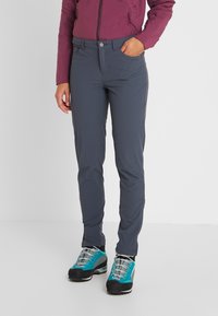 Grå prestationsbyxor med en slät textur och en åtsittande design. Tillsammans med blå och grå vandringsskor med distinkta snören och accenter.