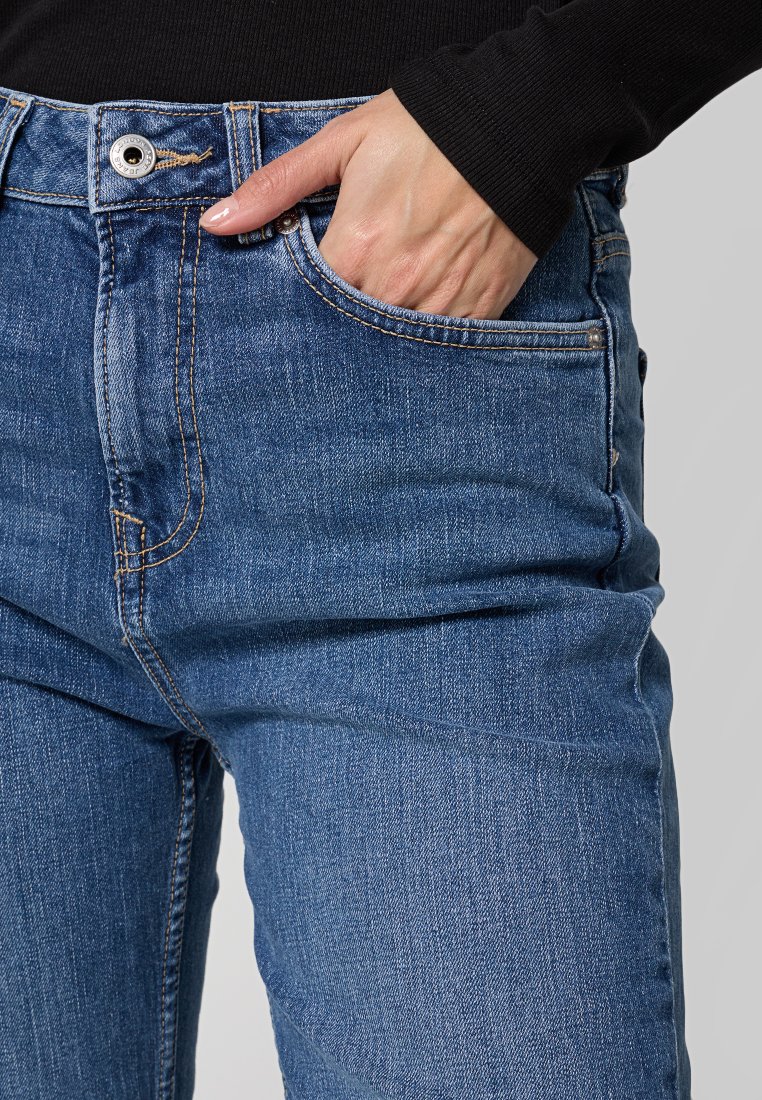 Jean en denim bleu avec une taille mi-haute, design à cinq poches, couture contrastante et coupe slim. Le tissu a une texture délavée.