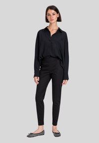 Camicia nera a maniche lunghe con bottoni e una tasca sul petto, abbinata a pantaloni neri su misura e ballerine nere a pois.