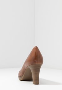 Scarpa alta in pelle marrone con punta affusolata e tacco in legno impilato, con una texture liscia e una silhouette leggermente curvata.