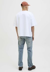 T-shirt en coton blanc oversize à manches courtes, associé à un jean en denim bleu clair et des chaussures à lacets marron. Casquette claire portée à l'envers.