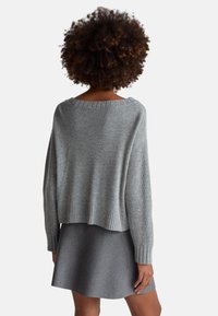 Grauer Strickpullover mit weitem Ausschnitt und geripptem Saum, kombiniert mit einem grauen ausgestellten Rock. Strukturierter Stoff, lockere Passform und lange Ärmel.