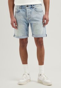 Hellblaue Denim-Shorts mit umgekrempelten Säumen, Fünf-Taschen-Design und subtiler Ausbleichung. Kombiniert mit weißen Turnschuhen und Socken.