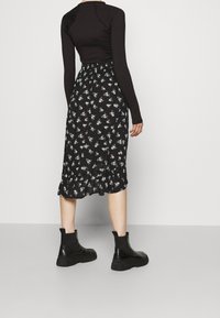 Musta pitkähihaine paita ja musta hame, jossa on kukkakuosi. Nilkkurit paksulla pohjalla, joissa on sileä ja teksturoitu pinta.