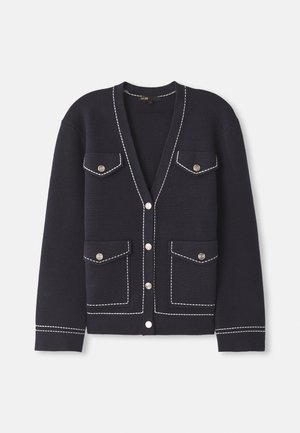 Marineblå cardigan laget av myk strikket stoff med kontrasterende hvite sømmer, med to frontlommer og runde sølvknapper.