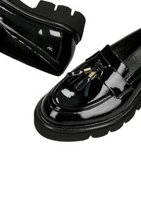 Zwarte lakleren loafers met een chunky zwarte zool, voorzien van franjes detail en gouden accenten op de bovenkant. Gladde, glanzende afwerking.