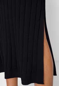 Abito a maglia nera a coste con uno spacco laterale, che crea un aspetto strutturato. L'orlo è dritto e il tessuto sembra morbido e flessibile.