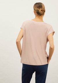 Světle růžový krátký rukáv top s volným střihem a kulatým výstřihem, v kombinaci s námořnickými pruhovanými kalhotami, z pohledu zezadu.
